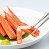 A serving of sliced carrots on a white plate with stainless steel chopsticks and a green leaf.