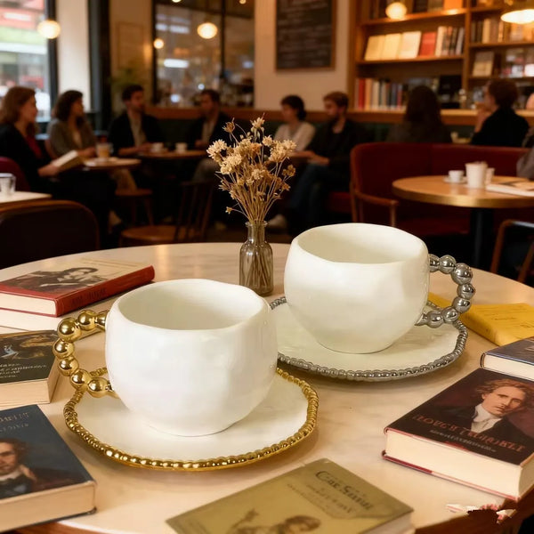 Weißer Keramiktasse und Untertasse mit Goldrand auf einem Holztisch.