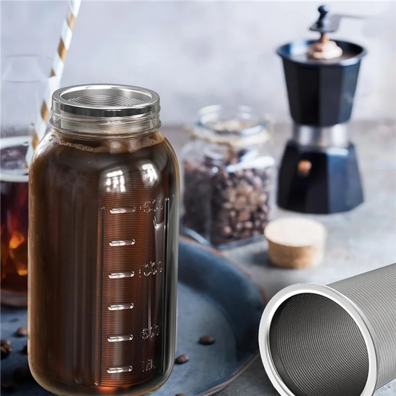 A glass jar filled with dark cold brew coffee sits next to a black coffee grinder and a metal filter.