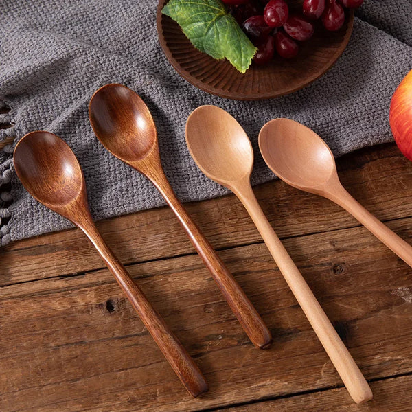 Ein Set aus natürlichen Holzlöffeln zum Suppen- und Kochbenutzen auf einem dunkelgrauen Tuch neben roten Früchten.