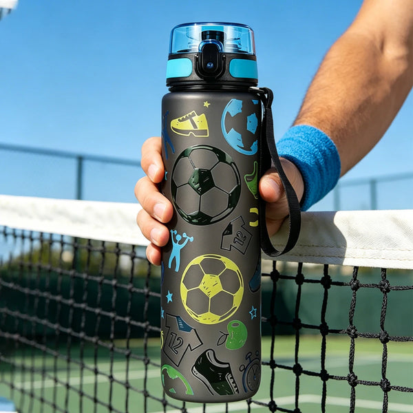 Eine Hand hält eine dunkelgraue, undurchlässige Wasserflasche mit Fußballmotiv, die verschiedene Fußballbälle und Schuhe zeig