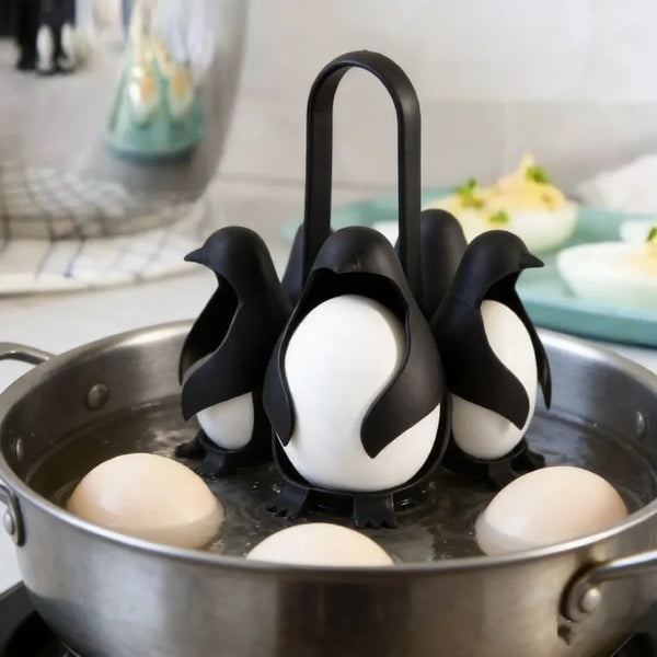 Schwarzes Pinguin-Eierkocher mit weißen Eiern in einem Metalltopf.
