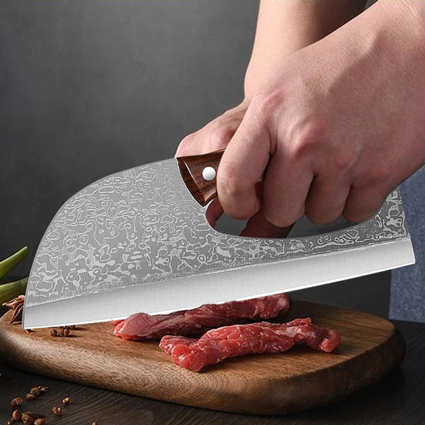 Eine Hand hält ein professionelles Edelstahl-Kochmesser über rotes Fleisch auf einem Holzbrett.
