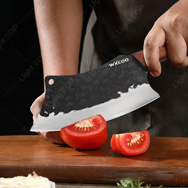 Eine Hand hält ein schwarzes, geschmiedetes Kochmesser mit weißer Klinge über einem Holzbrett.