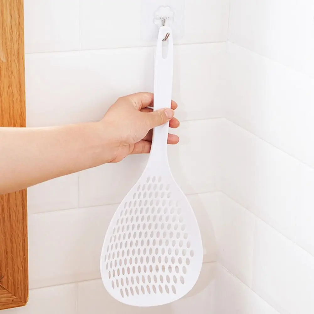 A hand is hanging a white kitchen strainer and skimmer set on a white tiled wall.