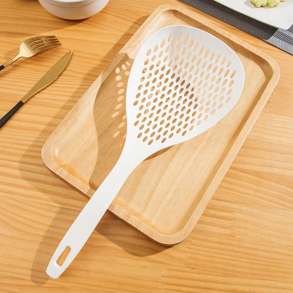 A white kitchen strainer and skimmer set rests on a wooden cutting board next to gold utensils.