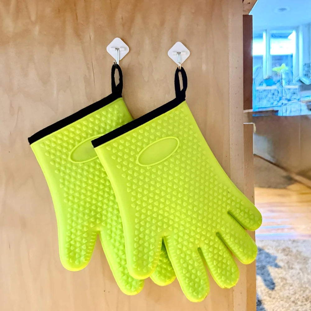 A pair of bright lime green silicone oven gloves hanging on a wooden surface.