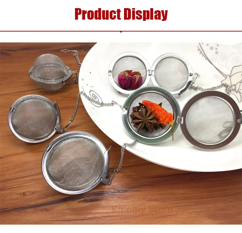 Stainless steel tea infuser balls with chains displaying loose leaf tea, spices, and herbs on a white plate.