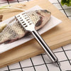 A stainless steel fish scale remover tool is shown next to a whole fish on a white plate.