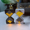 A pair of LED electronic hourglass timers, one black and one white, displaying yellow light.