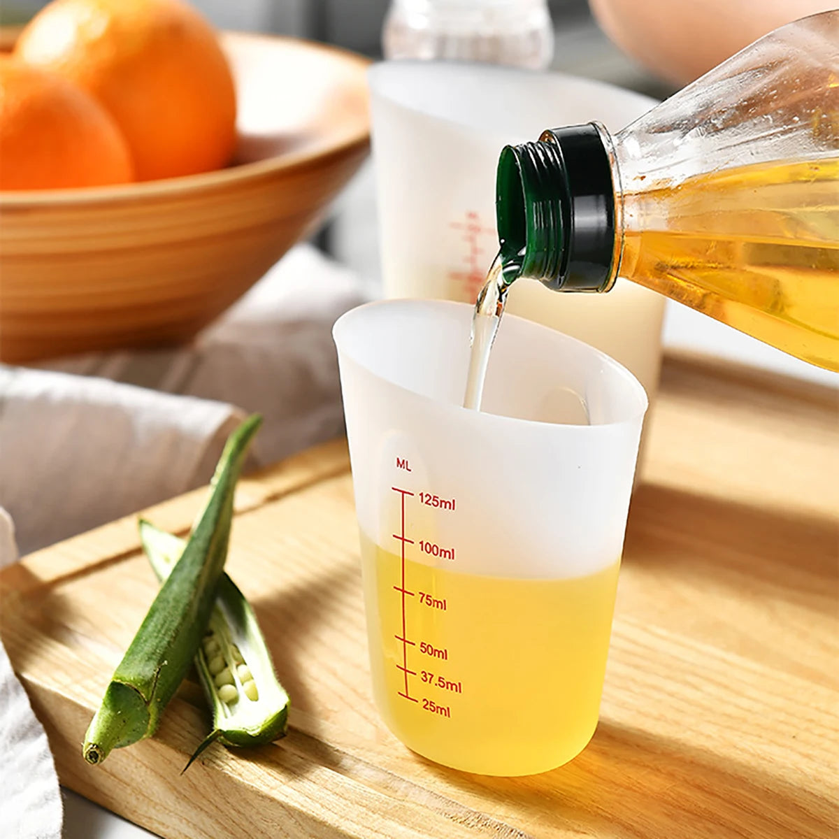 Une tasse à mesurer en silicone est remplie de liquide doré provenant d'une bouteille en verre sur une planche à découper en 