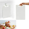A white plastic cutting board is hanging on a kitchen rack against a white subway tile background.