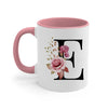 A pink ceramic coffee mug with a large black initial E decorated with floral greenery.