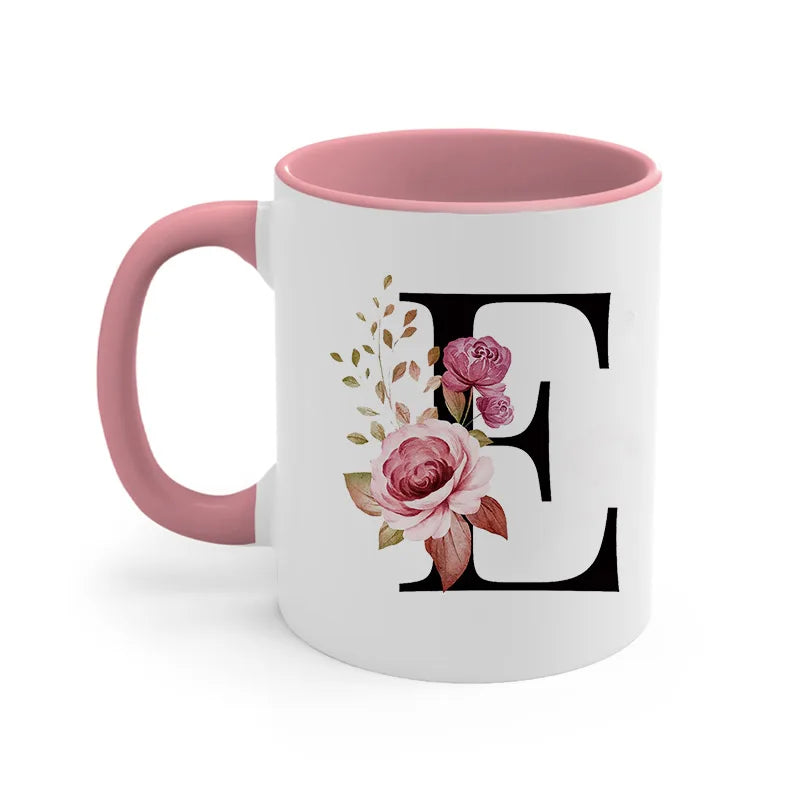 A pink ceramic coffee mug with a large black initial E decorated with floral greenery.