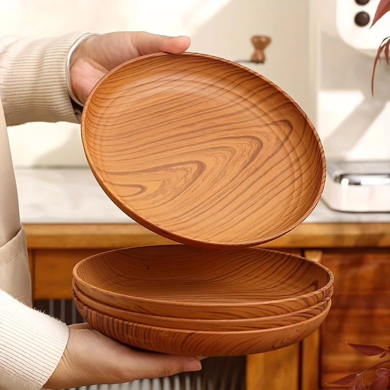 A hand holds a stack of round wooden serving trays with natural wood grain patterns.