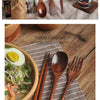 A set of natural wood dining utensils including a spoon, fork, knife, and chopsticks displayed on a wooden surface.