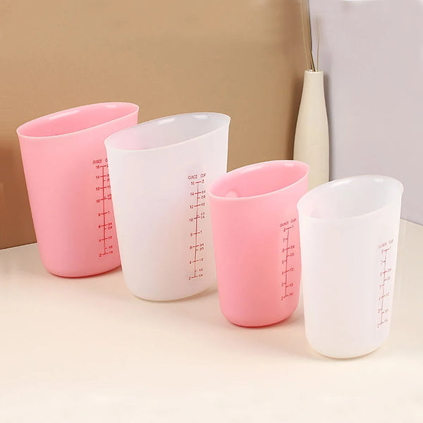 Drei Silikonmessbecher in rosa und weiß mit digitalen Waagen auf einer hellen Oberfläche.