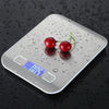 A silver digital kitchen scale rests on a dark surface with water droplets and a cherry.