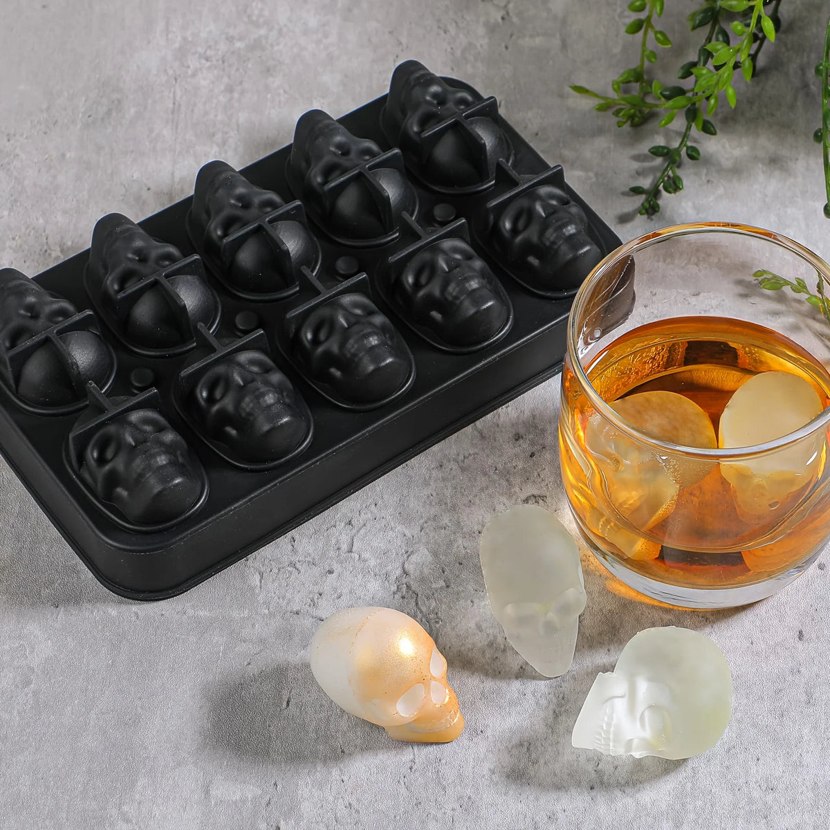 A black silicone mold tray filled with skull-shaped ice cube molds, alongside several finished translucent ice cubes.