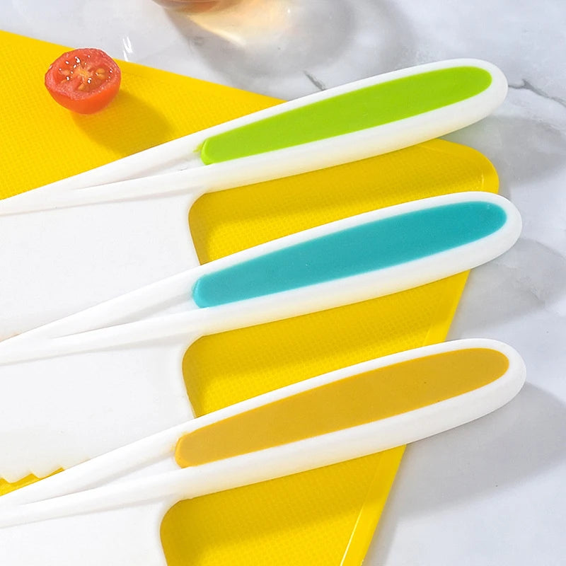 A set of plastic fruit and cake cutting tools in white with colored handles, resting on a yellow cutting board.