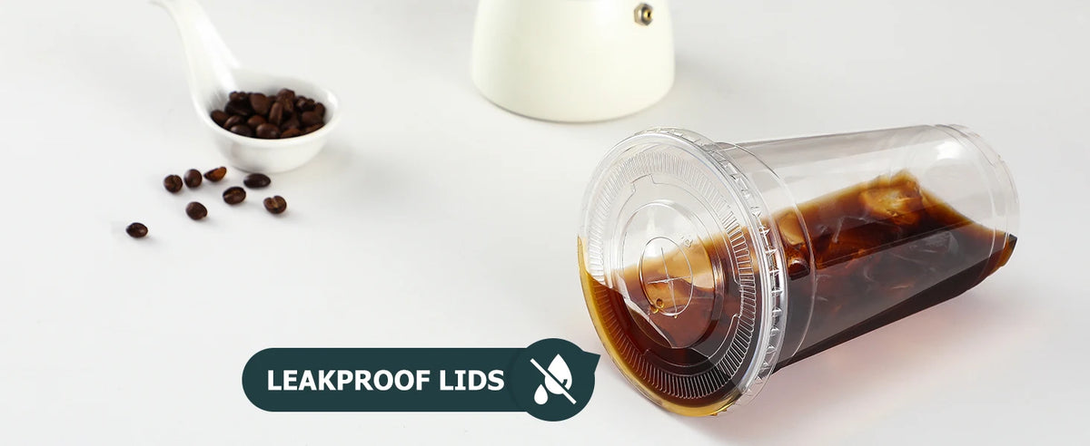 A clear plastic cup with a dark liquid and a lid is shown next to coffee beans and a white object.