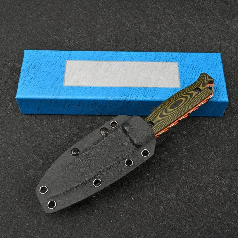 A black fixed blade outdoor camping knife rests on a dark surface next to a blue box.