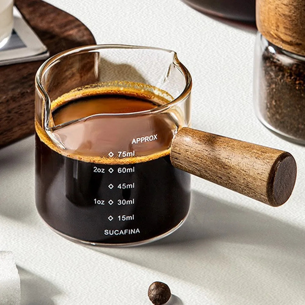 Una taza medidora de vidrio llena de líquido oscuro, mostrando marcas de volumen y un émbolo de madera.