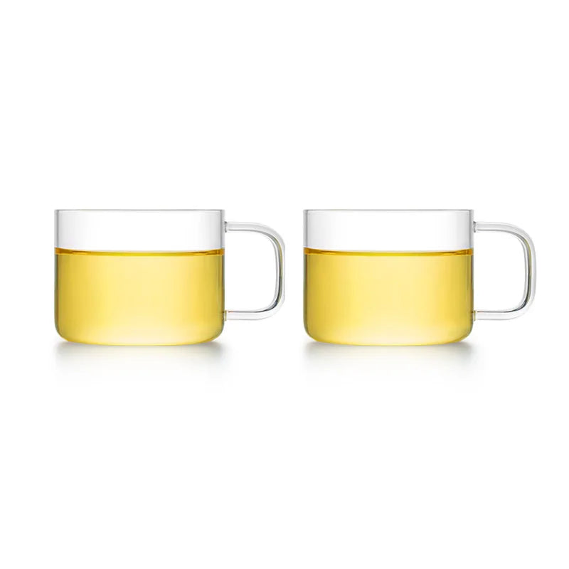 A set of two clear glass tea cups filled with yellow liquid on a white background.