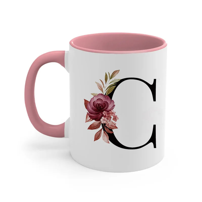 A pink ceramic coffee mug with a large black initial C decorated with floral leaves.