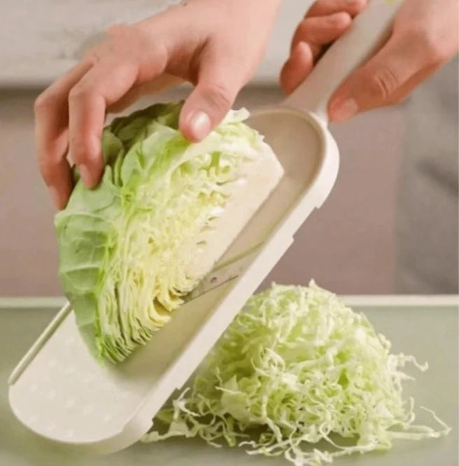 Hands are using a multi-function vegetable slicer to grate or slice a head of green cabbage.
