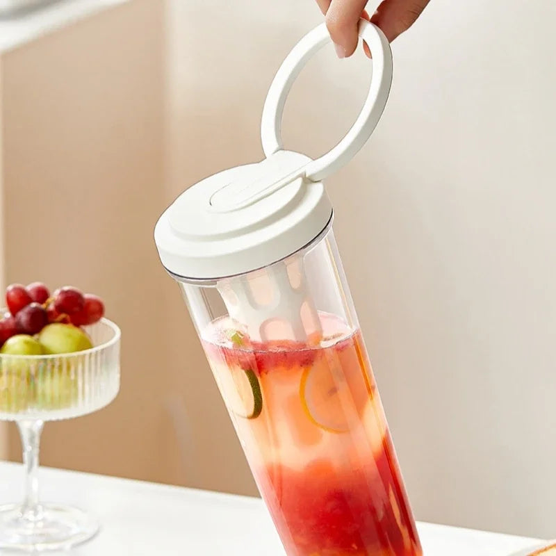 A hand is holding a clear glass jar with a white lid containing a red and orange beverage.