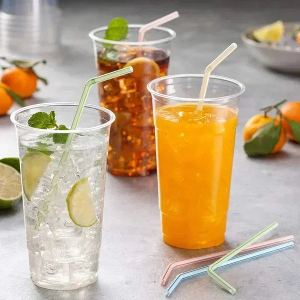 Ein Glas Orangensaft mit Strohhalm und Eis, neben anderen Getränken und Strohhalmen.