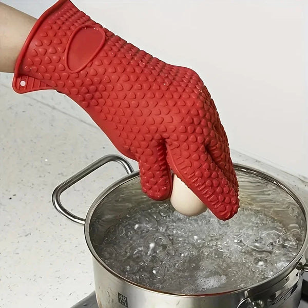 A red silicone heat resistant kitchen glove is shown dipping a white object into a pot of water.