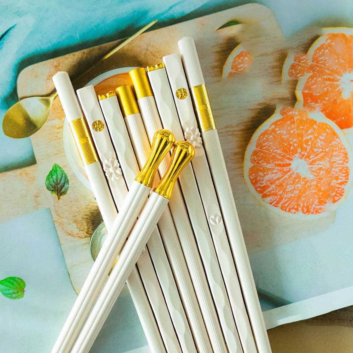 A set of five gold style chopsticks resting on a wooden board with orange slices.