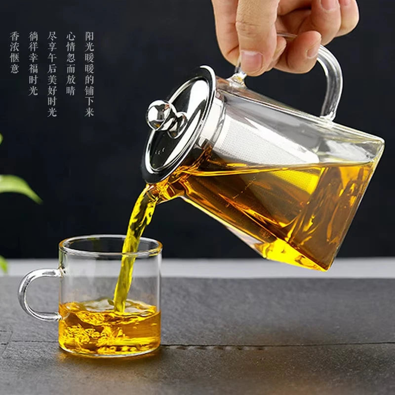A hand pours golden liquid from a heated glass teapot into a glass cup.
