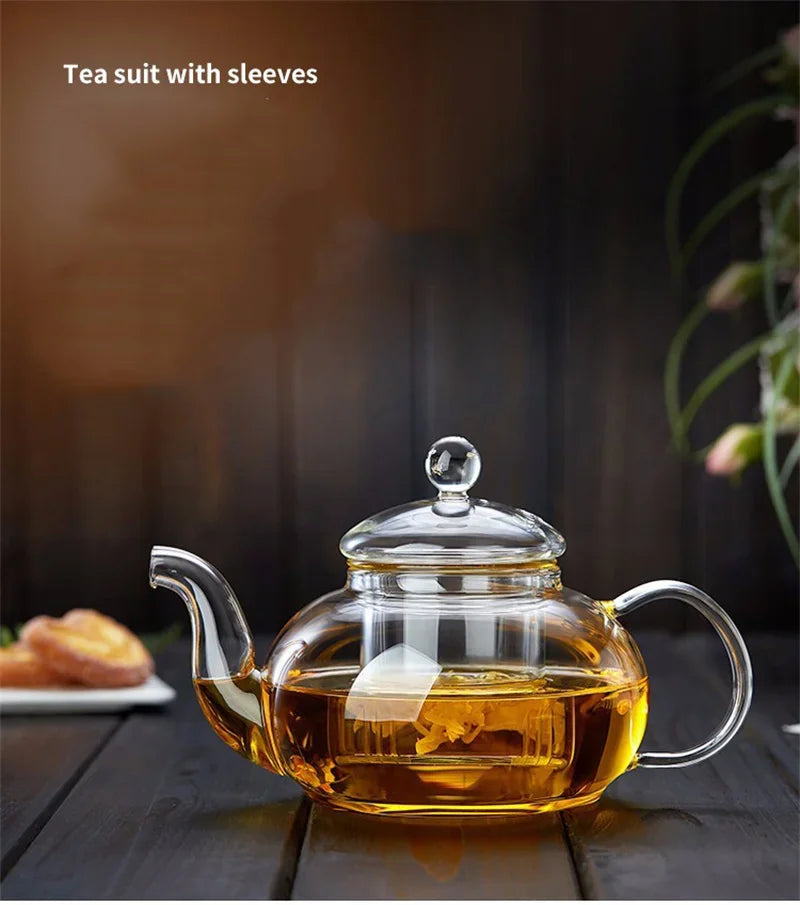 A clear glass tea pot with a lid and handle is filled with amber tea, sitting on a dark wooden surface.