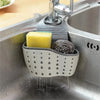 A close-up of an adjustable sink drain hanging sponge rack with a yellow sponge and a black scrubbing brush draining into the