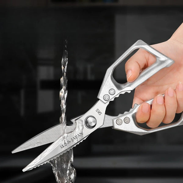 Eine Hand benutzt professionelle Titan-Küchenschere, um ein Stück Fleisch zu schneiden.