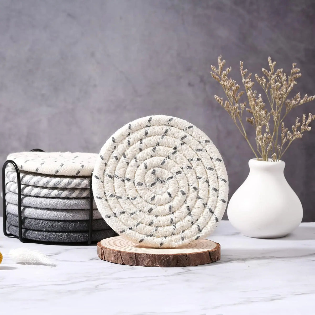 A set of eight round, textured cotton coasters with a gray and white pattern displayed on a white marble surface.