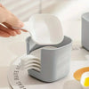 A hand is holding a white plastic sauce dish with a spoon, resting on a gray plastic dish set.