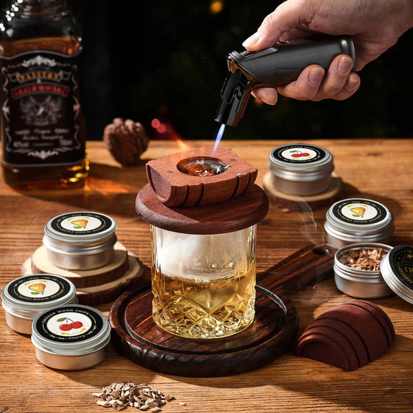 Eine Hand verwendet ein Rauchesgerät, um Whiskey in einem Glas zu verdampfen, umgeben von Holzspänen und Behältern.