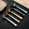 A collection of five stainless steel measuring scoops in various colors and finishes resting on a dark surface.