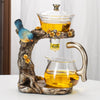 A decorative magnetic suction tea pot featuring a bird figurine and a glass teapot pouring golden tea.