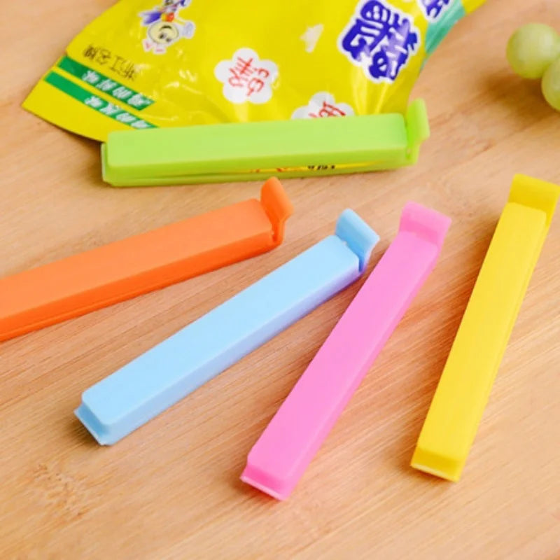 A collection of colorful reusable sealing clips in orange, light blue, pink, and yellow are displayed on a wooden surface.