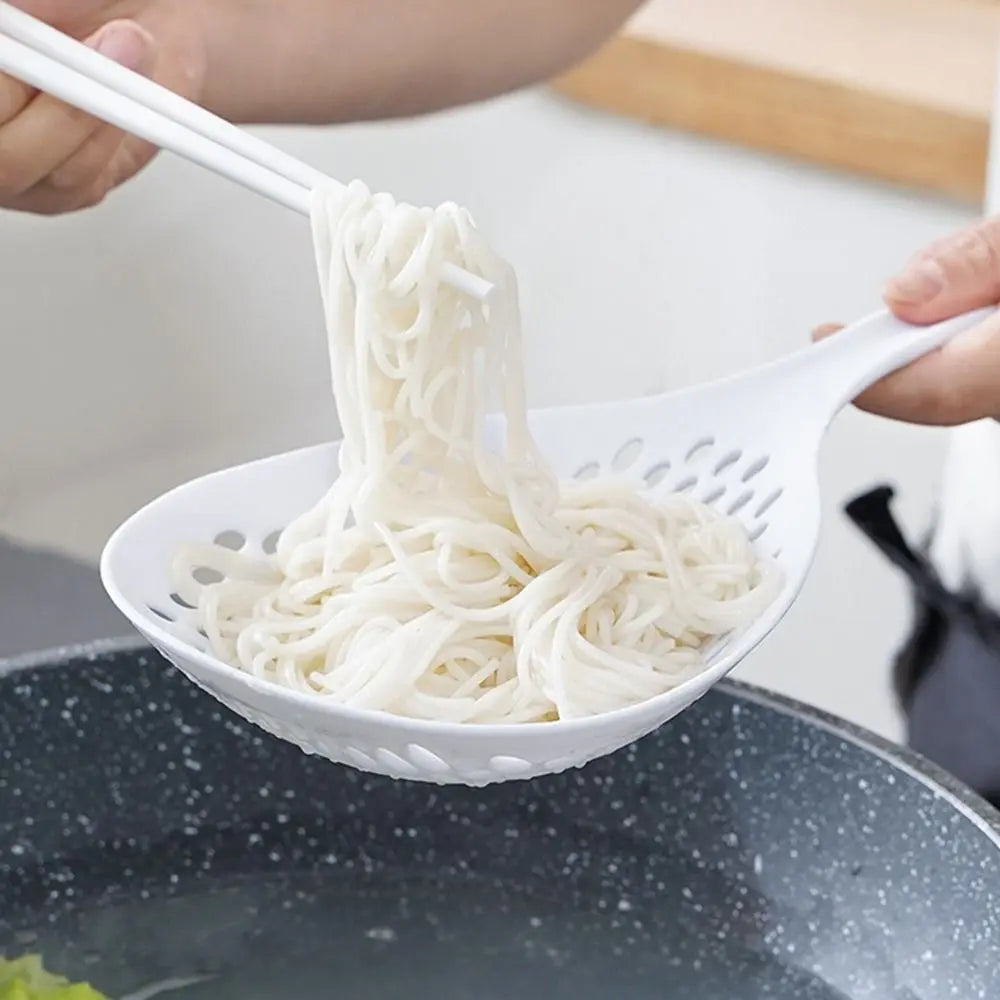 A hand is lifting a white kitchen strainer with noodles from a dark pot.