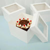White square disposable cake boxes with a chocolate cake decorated with cream and berries inside