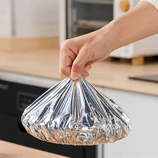 A hand is holding a clear aluminum foil food cover over a cooking appliance.