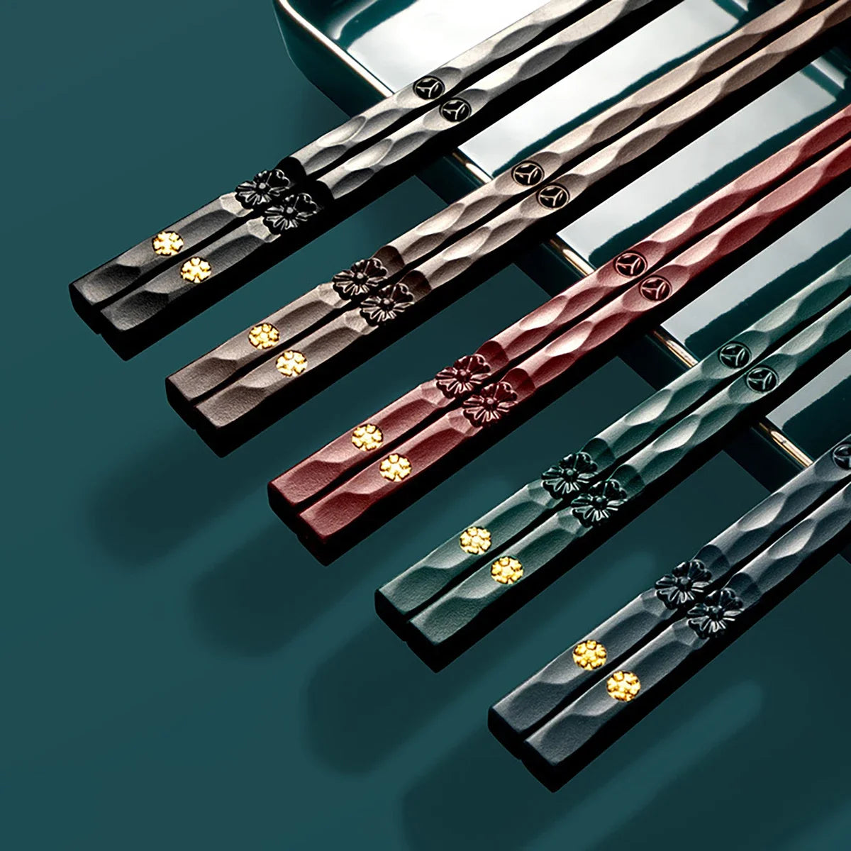 A set of five pairs of reusable food-grade metal chopsticks with various dark and reddish-brown finishes.