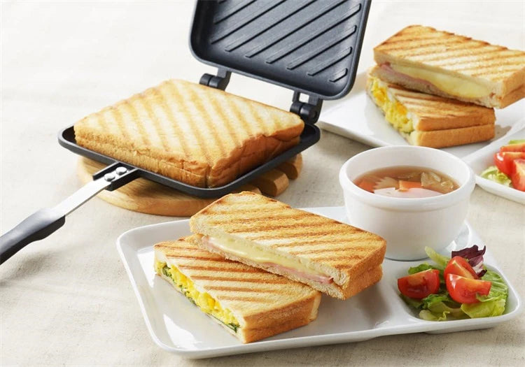 A non-stick sandwich and grill pan is shown with grilled sandwiches, bread, and a side of sauce and salad.