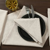 A set of decorative table napkins, a black plate, silverware, and a glass of amber liquid on a wooden table.